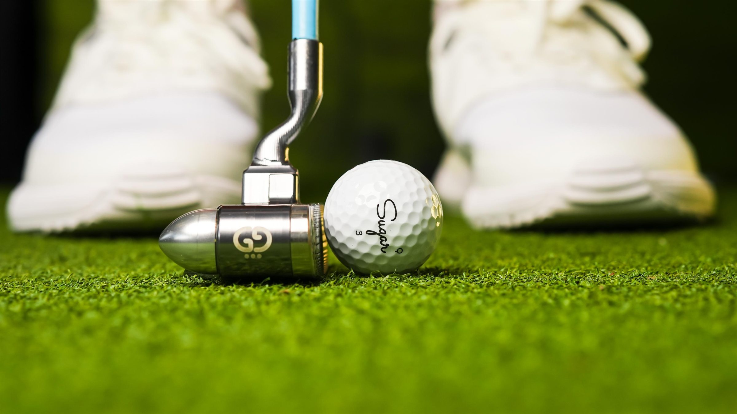A putter and a Sugar ball on the green, golfer standing over the shot