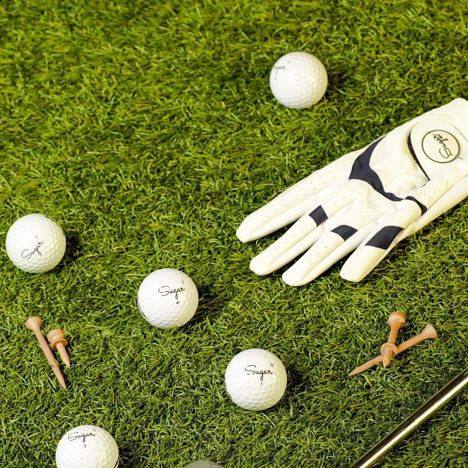 Flat lay on the grass: Sugar Golf glove, wooden tees, an iron and four Sugar balls