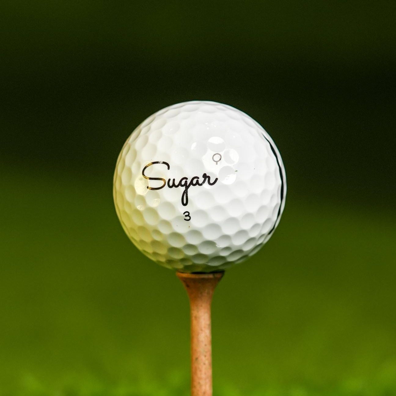 Sugar Quad golf ball teed up on the range, Q stamp beside the script logo