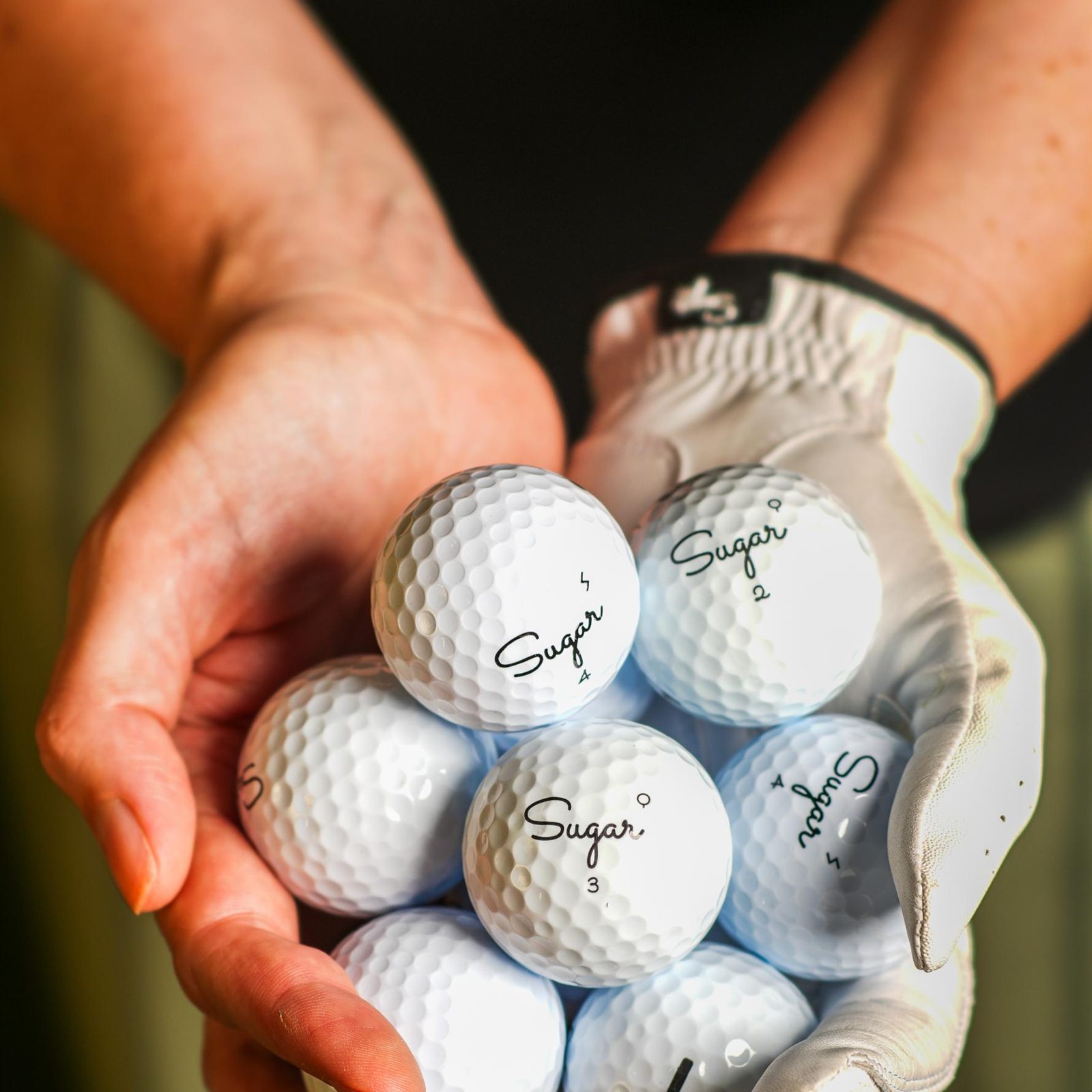 A gloved hand cradling a handful of Sugar golf balls