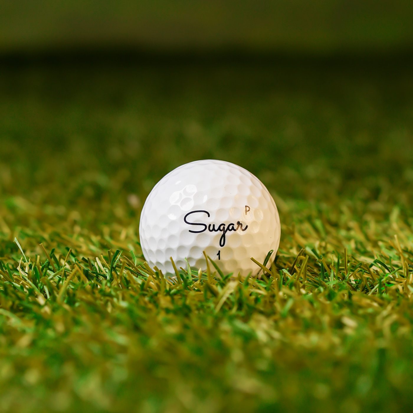 Sugar Pure golf ball low in the turf, P stamp beside the script logo
