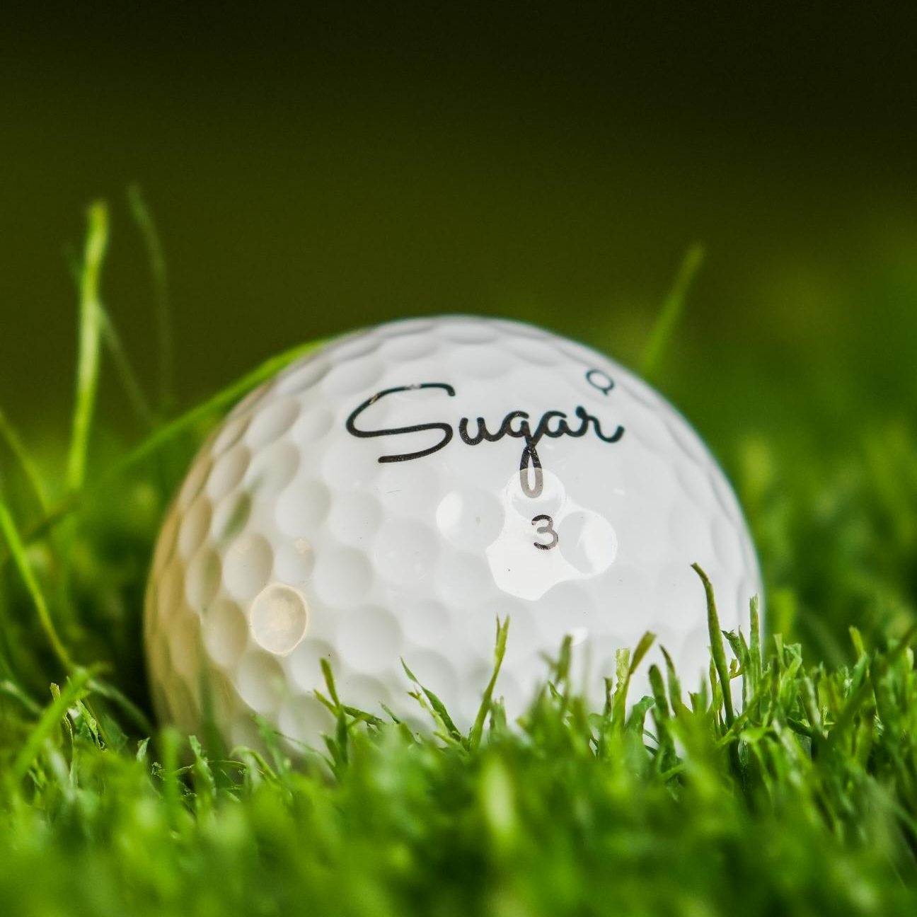 Sugar Quad golf ball nestled in the grass, Q stamp beside the script logo