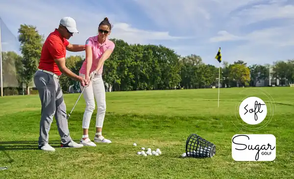 A beginner lady receiving a lesson from a golf coach on the range with low compression balls, showcasing the best soft golf balls for slow swing speeds.